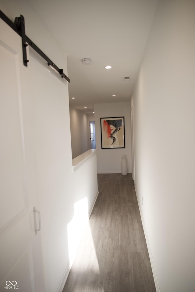 corridor featuring visible vents, baseboards, a barn door, recessed lighting, and wood finished floors