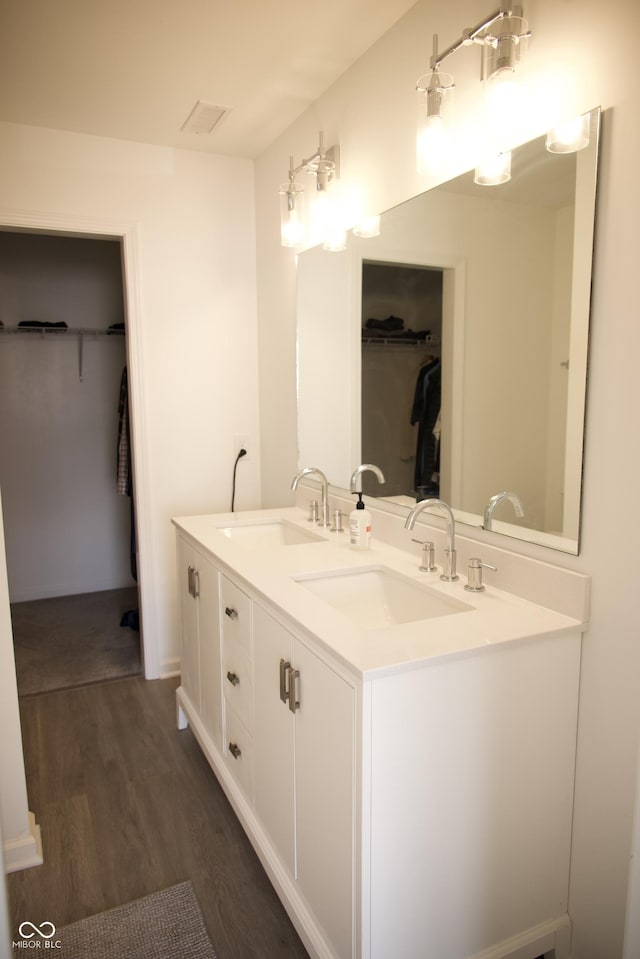 bathroom featuring a walk in closet, double vanity, wood finished floors, and a sink