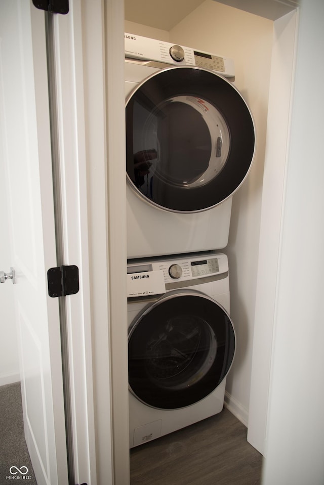 clothes washing area with baseboards, stacked washer and dryer, wood finished floors, and laundry area