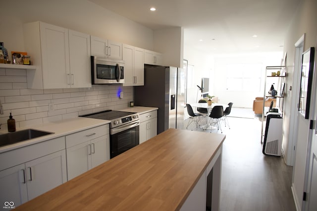 kitchen with a sink, stainless steel appliances, white cabinets, tasteful backsplash, and butcher block counters