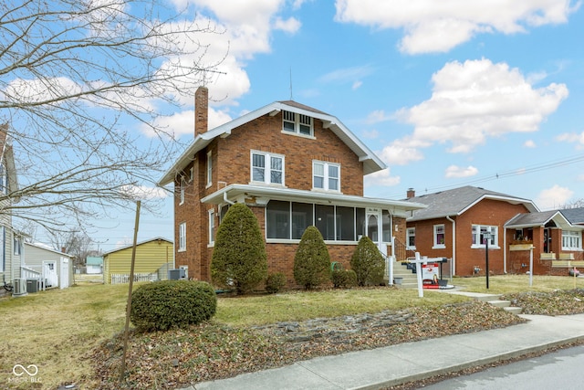 view of front of home with central AC unit, a sunroom, a chimney, a front lawn, and brick siding