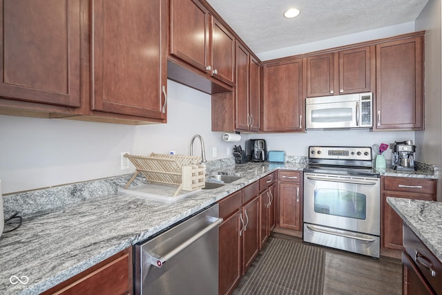 kitchen with light stone countertops, dark wood finished floors, stainless steel appliances, a textured ceiling, and a sink