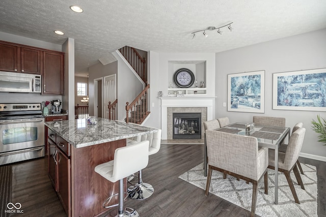 kitchen with dark wood finished floors, a tiled fireplace, a breakfast bar, appliances with stainless steel finishes, and a textured ceiling