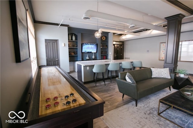 playroom featuring visible vents, a sink, light wood-style floors, a community bar, and decorative columns