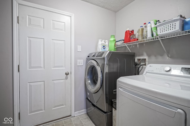 washroom featuring laundry area, washer and dryer, a textured ceiling, and baseboards