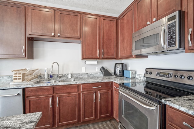 kitchen featuring a sink, a textured ceiling, light stone counters, and stainless steel appliances