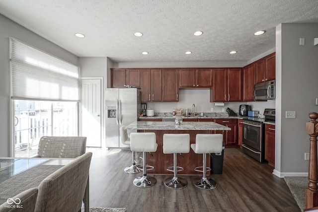 kitchen featuring a kitchen island, a breakfast bar, a sink, stainless steel appliances, and dark wood-type flooring