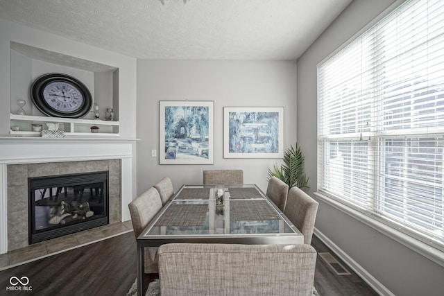 dining room with visible vents, a textured ceiling, wood finished floors, baseboards, and a tile fireplace