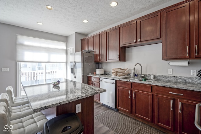 kitchen featuring light stone counters, stainless steel appliances, a kitchen bar, and a sink