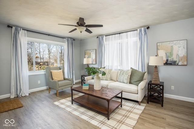 living area featuring light wood finished floors, a ceiling fan, and baseboards