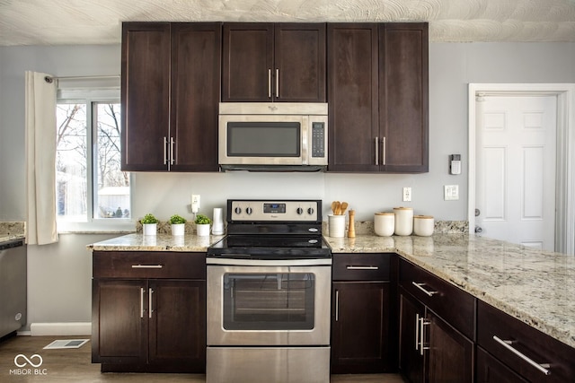 kitchen featuring stainless steel appliances, light stone countertops, and dark brown cabinetry