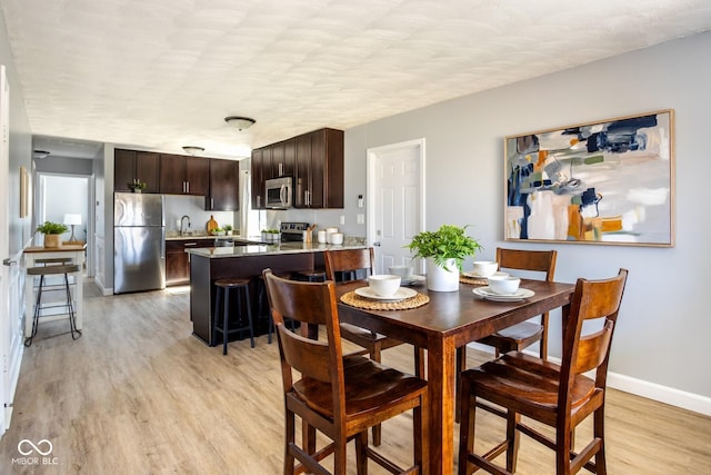 dining space with light wood finished floors, a textured ceiling, and baseboards