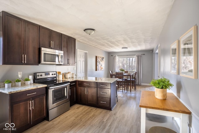 kitchen with light stone counters, a peninsula, light wood-style flooring, dark brown cabinets, and appliances with stainless steel finishes