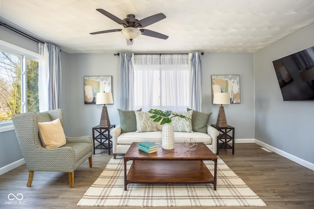 living room with ceiling fan, baseboards, and wood finished floors