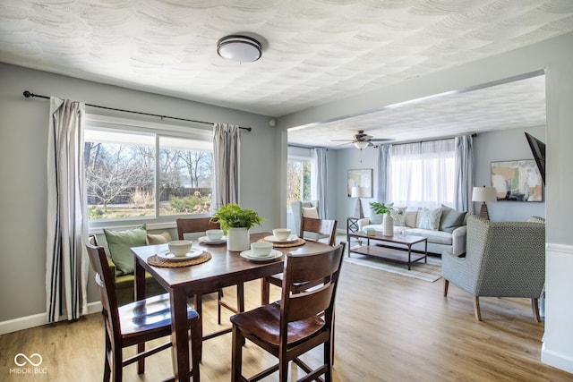 dining area featuring ceiling fan, light wood-style flooring, baseboards, and a textured ceiling