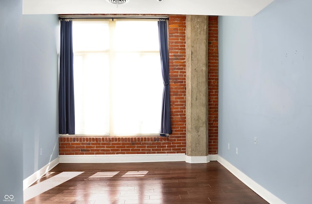 unfurnished room with brick wall, wood finished floors, visible vents, and baseboards