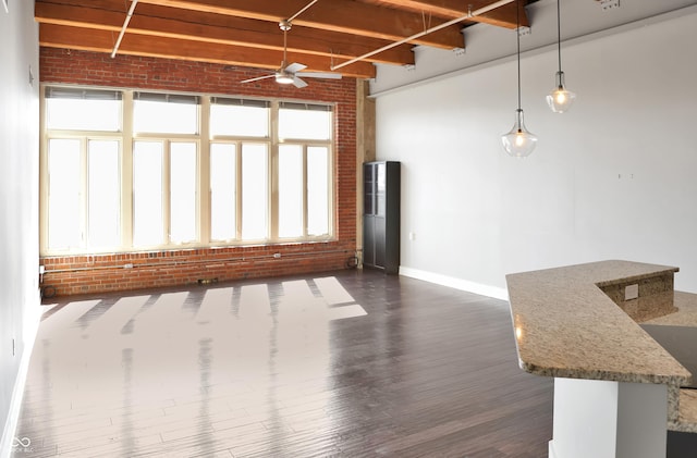 unfurnished living room featuring brick wall, a ceiling fan, baseboards, beam ceiling, and dark wood finished floors