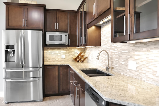 kitchen with light stone counters, dark brown cabinetry, a sink, appliances with stainless steel finishes, and backsplash