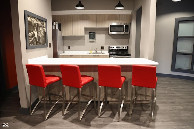 kitchen featuring a breakfast bar area, stainless steel appliances, wood finished floors, light countertops, and decorative light fixtures