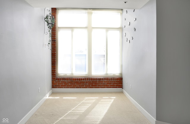 carpeted spare room with brick wall and baseboards