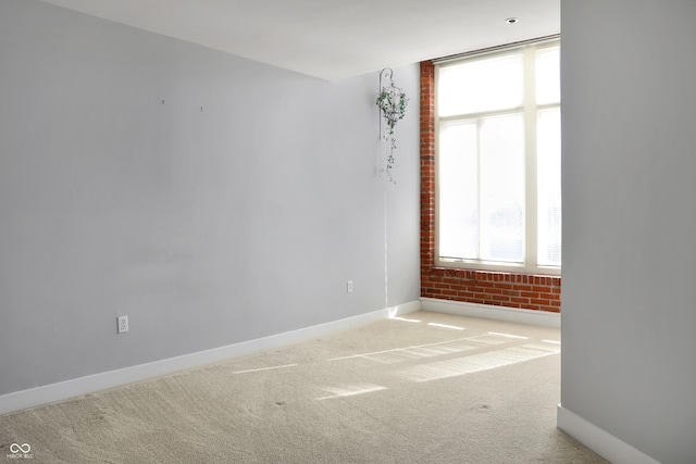 spare room featuring carpet floors, brick wall, and baseboards