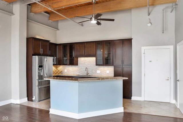 kitchen featuring light stone counters, beamed ceiling, stainless steel appliances, dark brown cabinets, and a sink