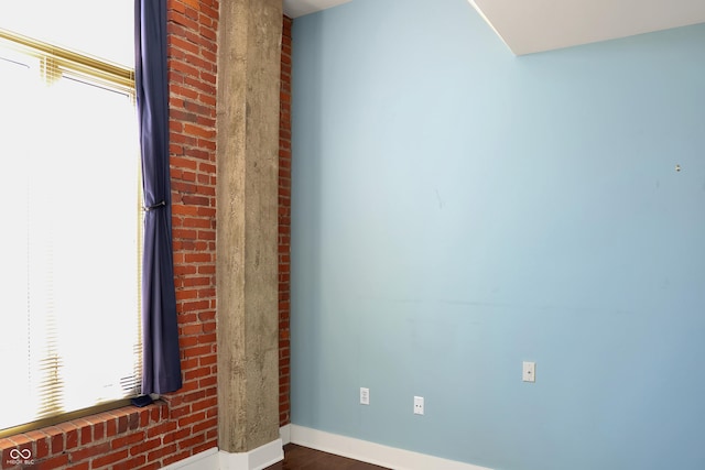 spare room with brick wall, dark wood-style flooring, plenty of natural light, and baseboards