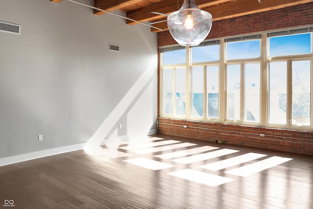 unfurnished room featuring visible vents, beamed ceiling, hardwood / wood-style floors, and brick wall