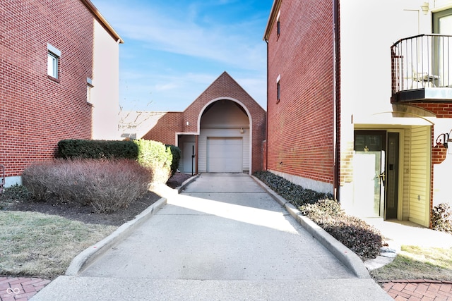 exterior space featuring a garage, a balcony, concrete driveway, and brick siding