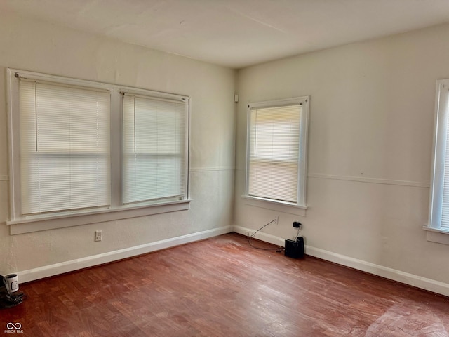 empty room with wood finished floors, a wealth of natural light, and baseboards