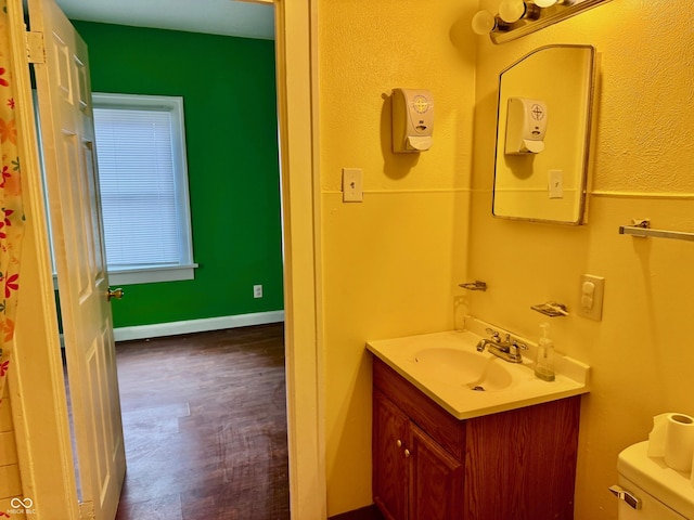 bathroom featuring toilet, baseboards, wood finished floors, and vanity