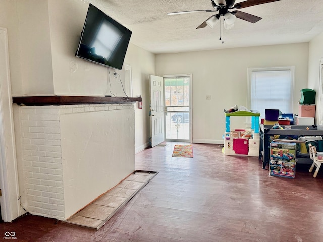 interior space featuring a ceiling fan, a textured ceiling, baseboards, and wood finished floors