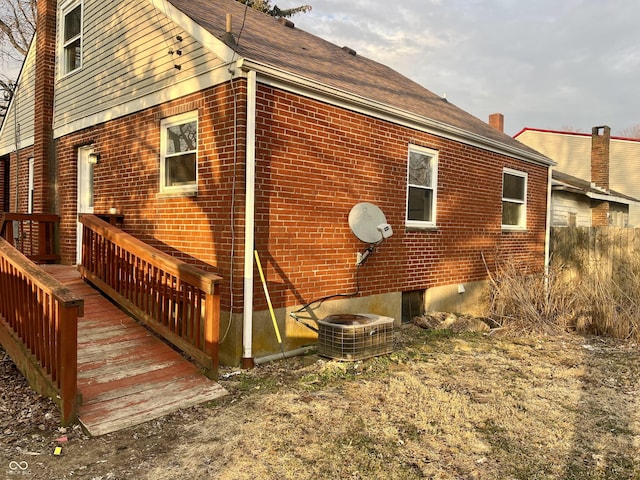 view of property exterior with brick siding, a chimney, and central air condition unit