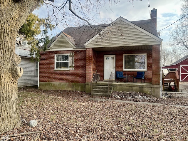 bungalow featuring brick siding, a chimney, and roof with shingles