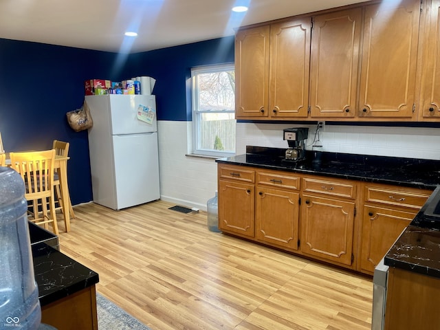 kitchen with light wood-style flooring, brown cabinetry, wainscoting, and freestanding refrigerator