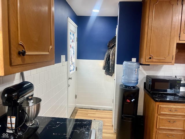 kitchen with black microwave, light wood-style flooring, tile walls, wainscoting, and brown cabinetry