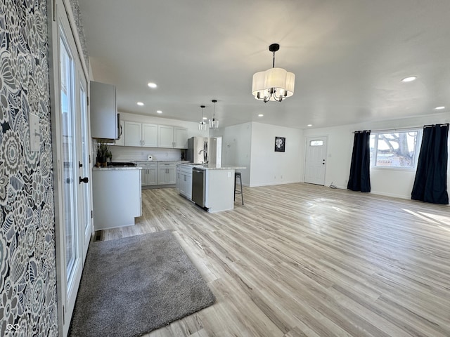 kitchen with light countertops, hanging light fixtures, appliances with stainless steel finishes, open floor plan, and light wood-type flooring