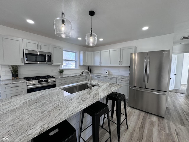 kitchen featuring light wood-style flooring, a sink, a kitchen breakfast bar, appliances with stainless steel finishes, and light stone countertops