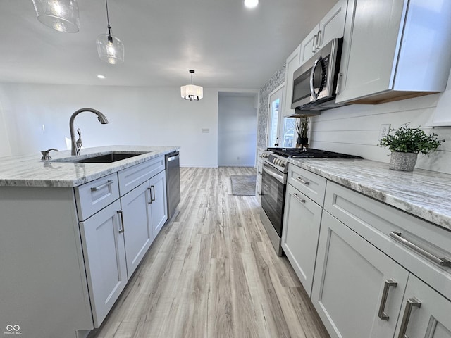 kitchen featuring light stone counters, stainless steel appliances, a sink, light wood-style floors, and pendant lighting