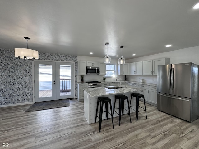 kitchen featuring french doors, a breakfast bar area, appliances with stainless steel finishes, a kitchen island with sink, and a sink