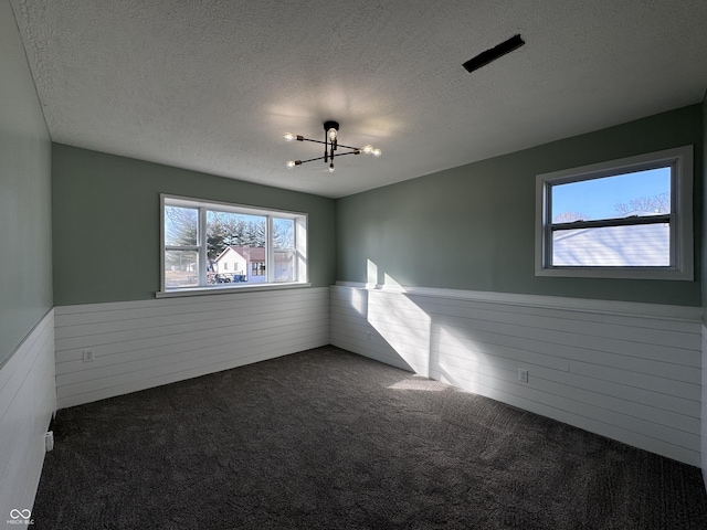 unfurnished room featuring a wainscoted wall, a textured ceiling, and dark carpet