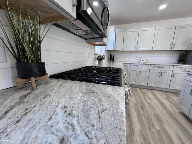 kitchen with stainless steel appliances, light wood-style floors, decorative backsplash, and light stone countertops