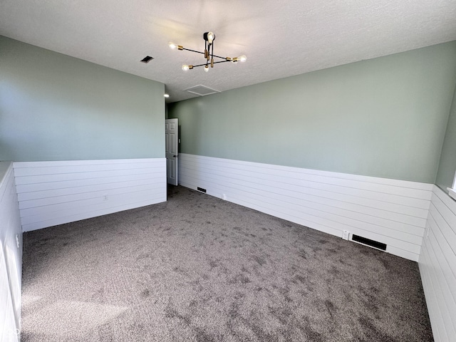 unfurnished room featuring a wainscoted wall, visible vents, an inviting chandelier, carpet flooring, and a textured ceiling