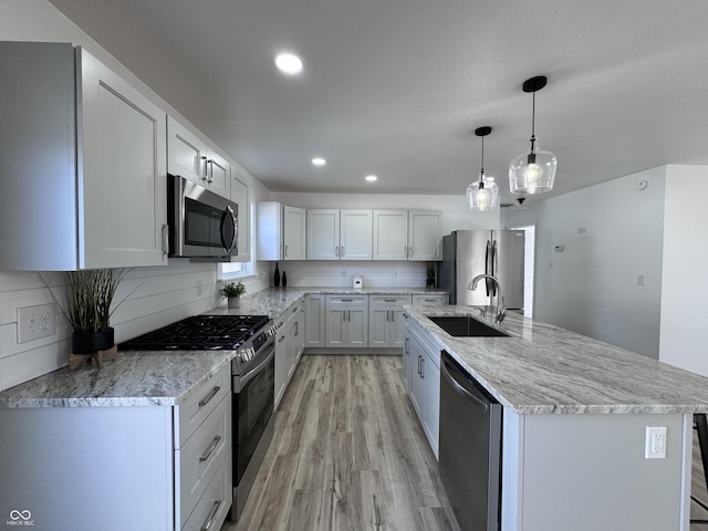 kitchen with stainless steel appliances, a sink, light wood-type flooring, decorative backsplash, and light stone countertops