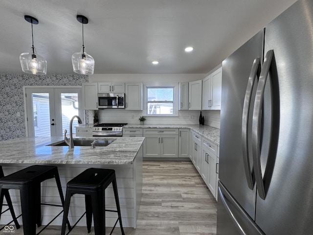 kitchen with light stone counters, french doors, a breakfast bar area, stainless steel appliances, and a sink