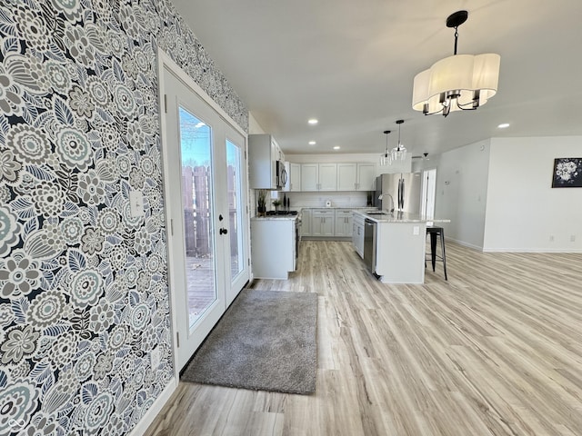 kitchen featuring baseboards, appliances with stainless steel finishes, a breakfast bar area, light countertops, and light wood-style floors