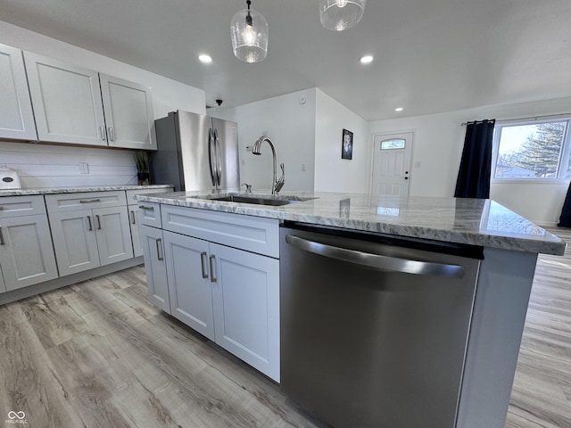 kitchen with light wood-style flooring, light stone countertops, stainless steel appliances, pendant lighting, and a sink