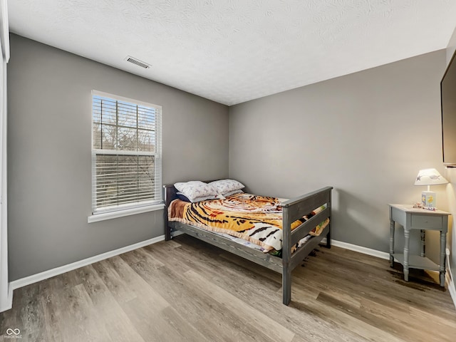 bedroom featuring visible vents, baseboards, a textured ceiling, and wood finished floors