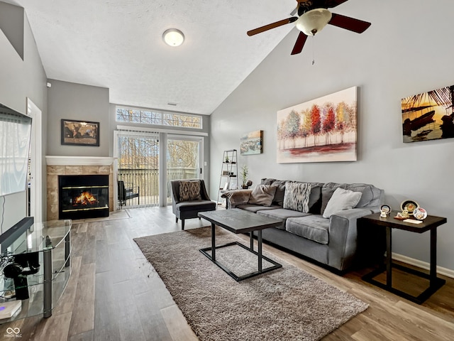 living area featuring wood finished floors, baseboards, high vaulted ceiling, a fireplace, and a textured ceiling