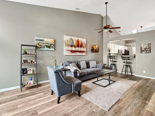 living room featuring baseboards, light wood-style floors, ceiling fan, and high vaulted ceiling